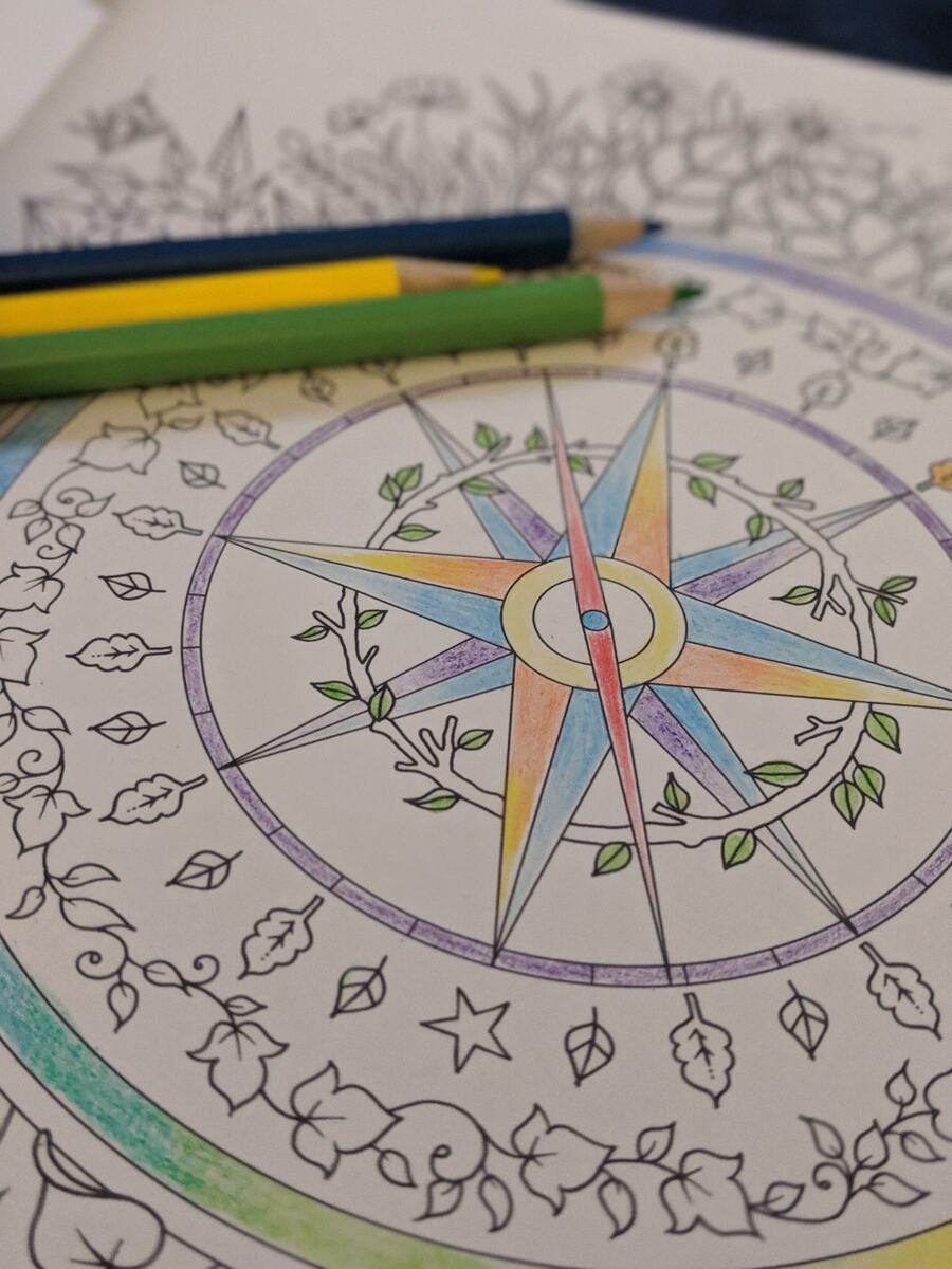 A compass-rose mandala being colored in with pencils