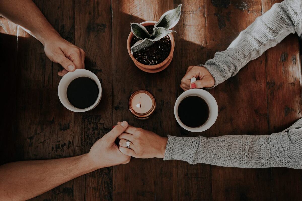 Two people holding hands across a table with cups of coffee