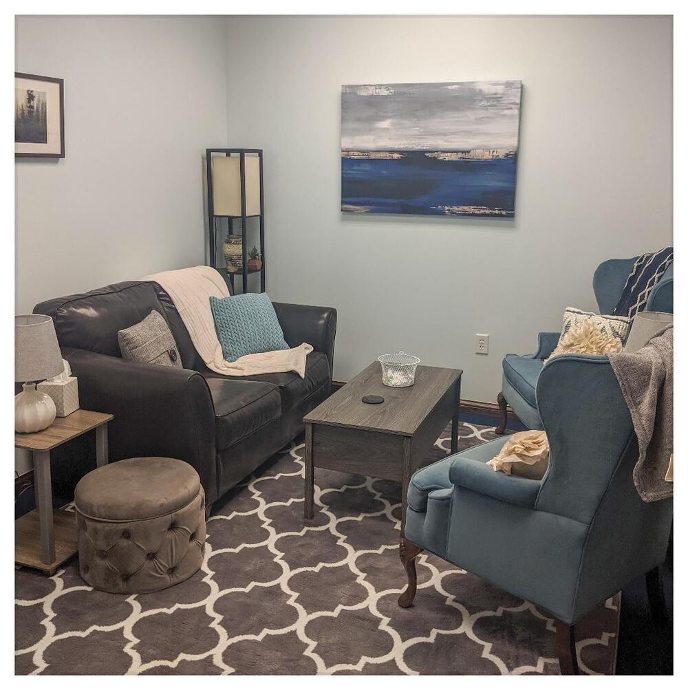 The counseling office: a leather loveseat with throw pillows, two blue armchairs and a coffee table on a patterned rug
